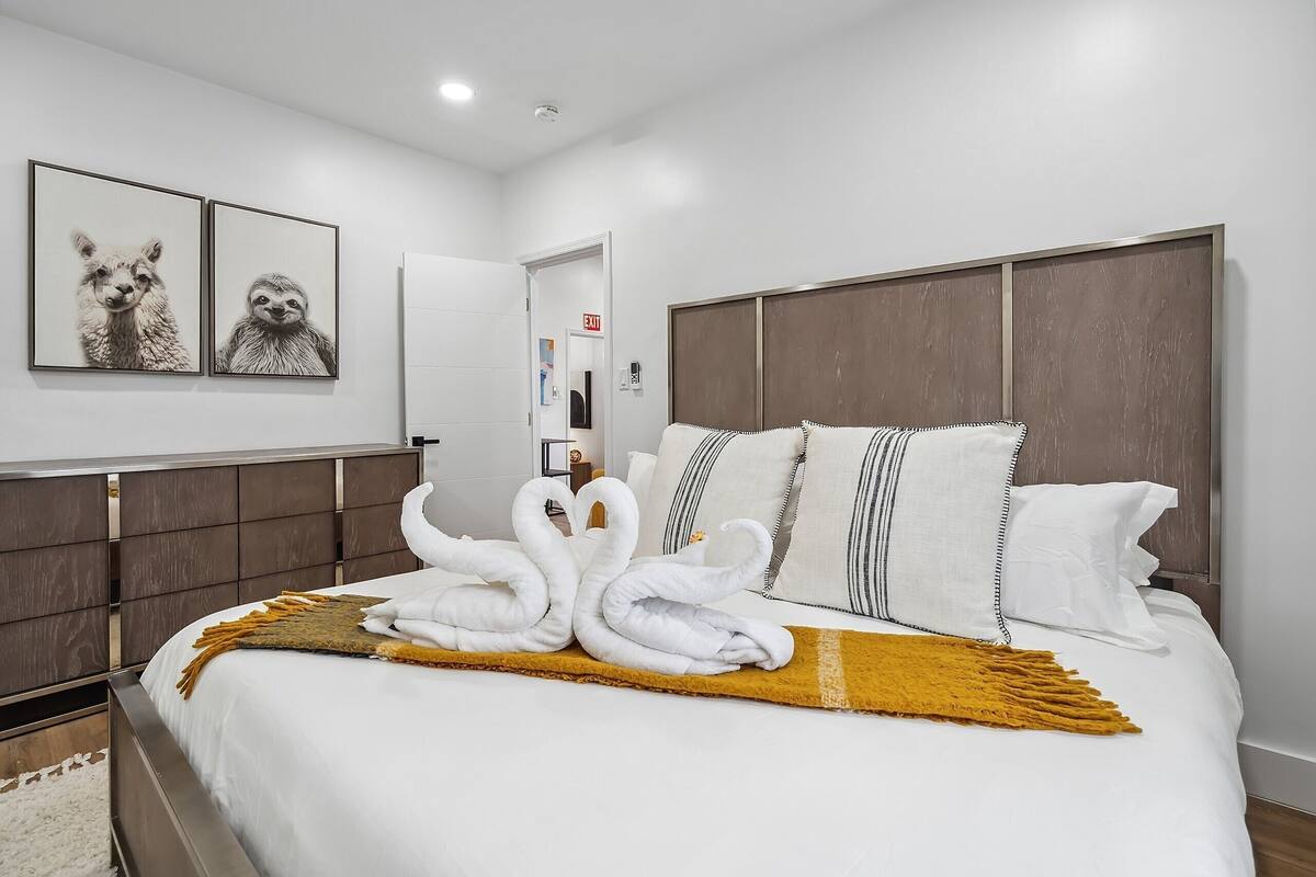 A modern hotel room with a neatly made bed, a headboard with a wooden panel, and two framed animal pictures on the wall.