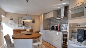 A modern kitchen with white cabinets, a round wooden table, and a built-in oven. - End Barn at Blackclough Farm (Buxton)