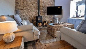 A cozy living room with a stone wall, a fireplace, a flat-screen TV, and comfortable seating. - End Barn at Blackclough Farm (Buxton)