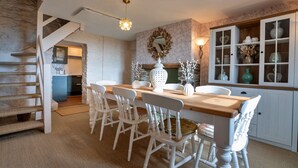 A dining area with a wooden table and white chairs, a staircase, and a cabinet with glass doors.