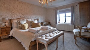 A bedroom with a large bed, a bench, a nightstand, a dresser, and a window with curtains.