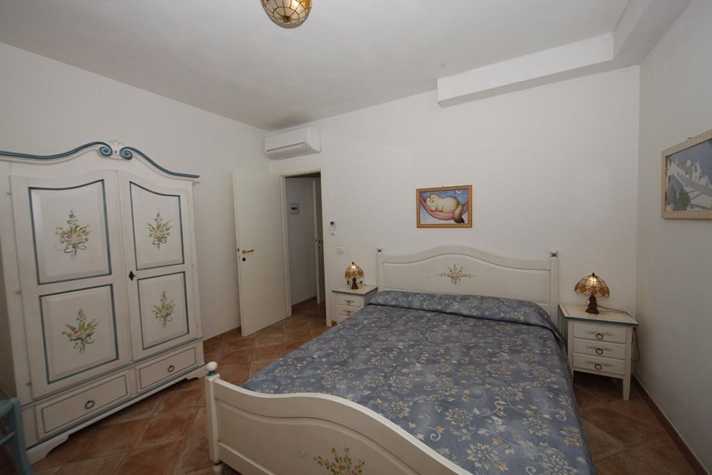 Un dormitorio con cama, armario, mesita de noche y un cuadro en la pared.