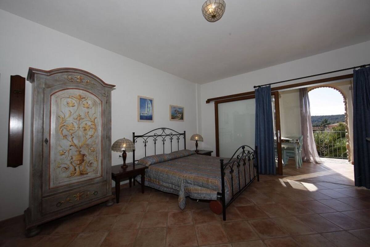 A bedroom with a bed, a wardrobe, a nightstand, and a view of the outdoors.
