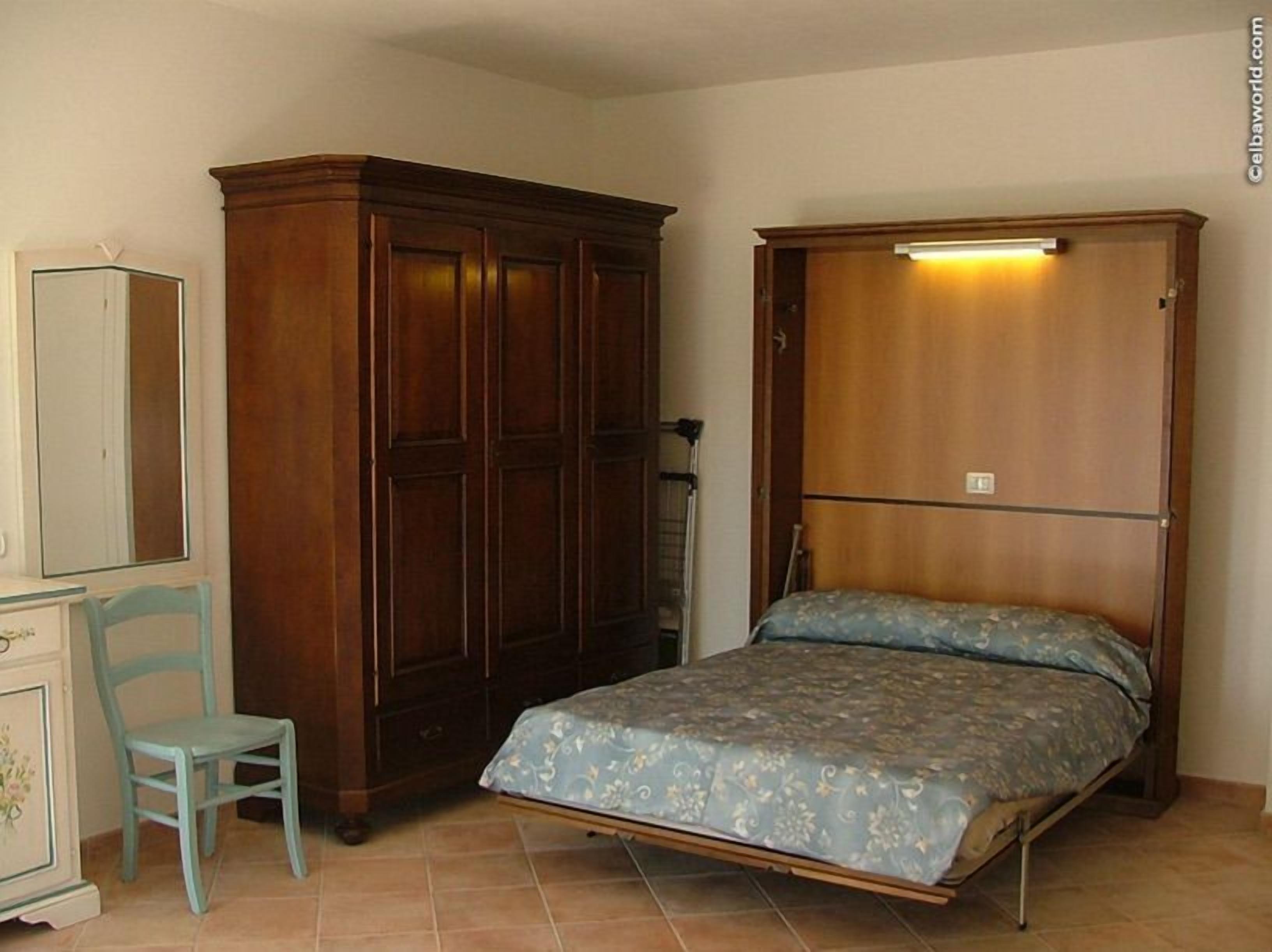 Un dormitorio con cama, armario de madera, una silla y cómoda.