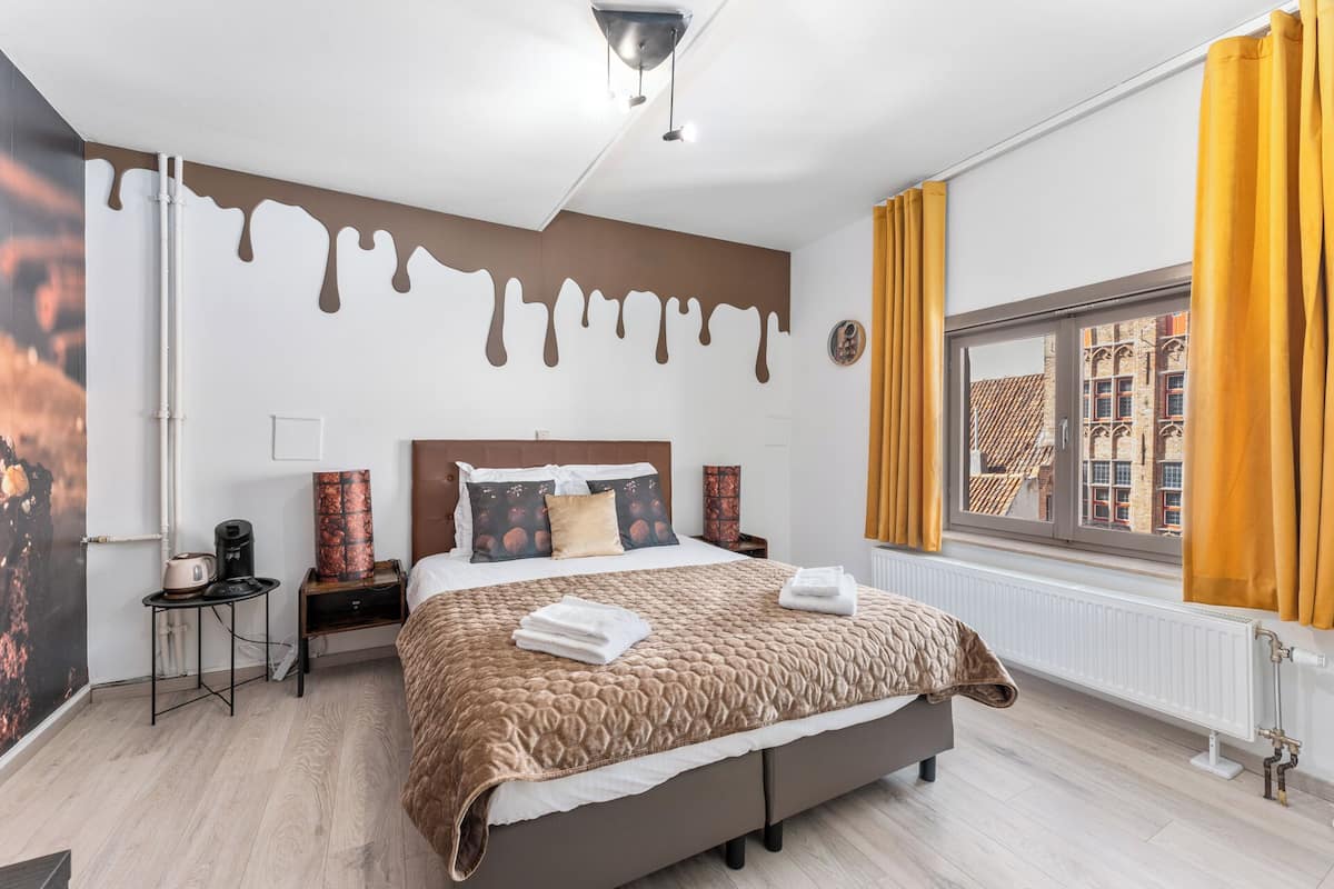 A modern hotel room with a large bed, a nightstand, a coffee machine, and a window with curtains.