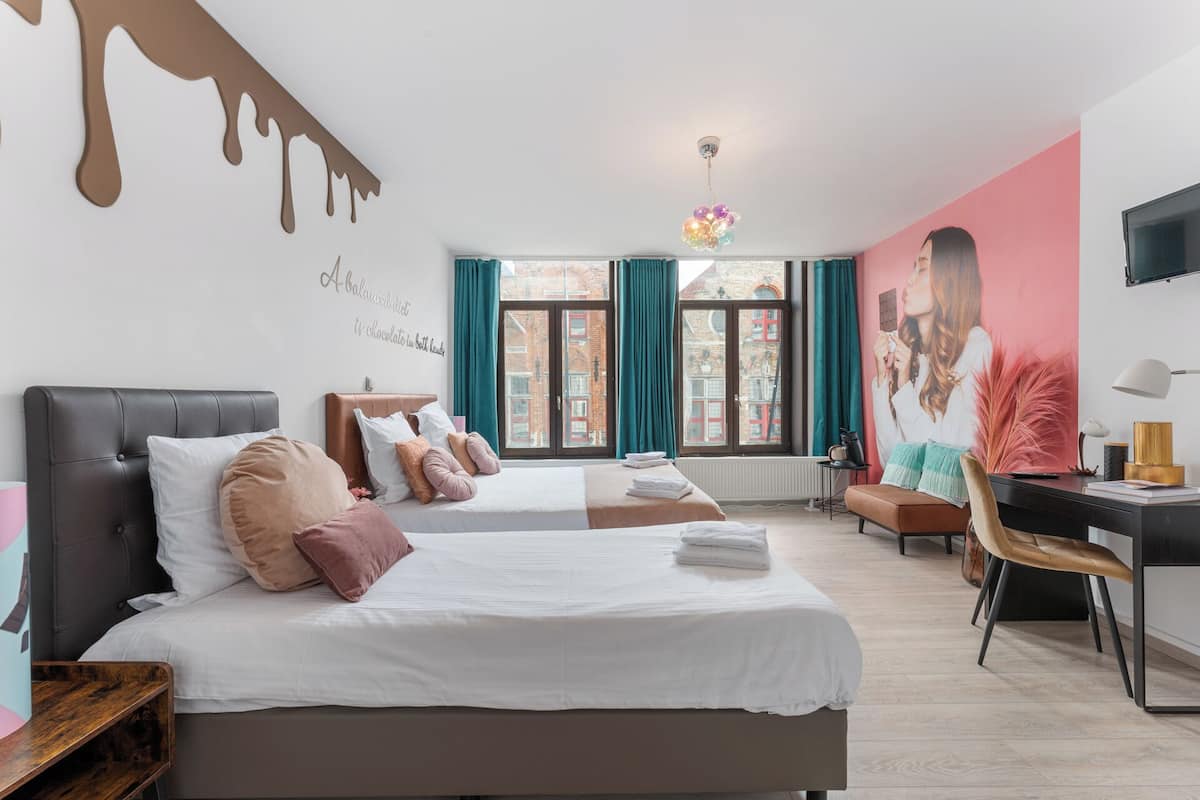 A hotel room with two beds, a desk, a chair, and a large window with curtains.