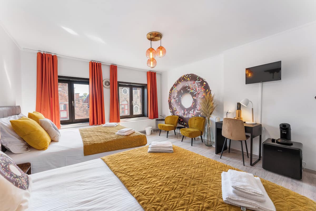 A hotel room with two beds, a desk, a chair, a TV, and a large donut decoration.