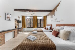 Een hotelkamer met een haard van baksteen, twee bedden met bruin-witte beddengoed, een groot raam met gordijnen en een muur met een citaat over chocolade.