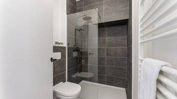 Une salle de bain moderne avec une douche à parois de verre, des toilettes blanches et un porte-serviettes blanc.