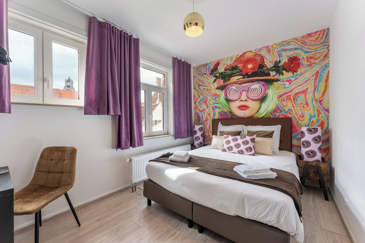 A modern bedroom with a large bed, a chair, and a colorful mural on the wall.