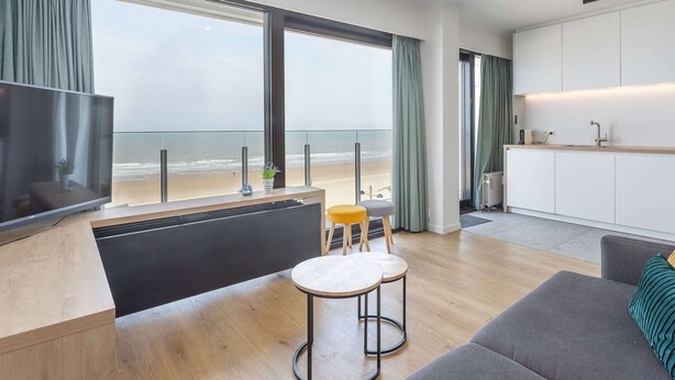 A modern living room with a large TV, a sofa, and a dining area with a small table and chairs. - Amazing Apartment With Sea-views (Middelkerke)