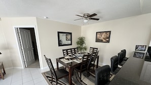 A dining area with a table set for four, surrounded by chairs, a ceiling fan, and framed pictures on the walls. - Villa Crayson (Kissimmee)