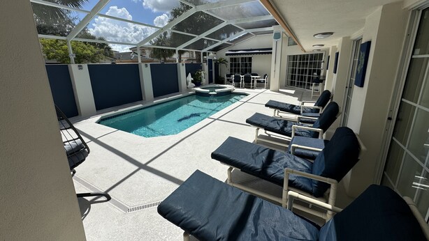 A covered outdoor swimming pool area with lounge chairs and a patio table. - Villa Crayson (Kissimmee)