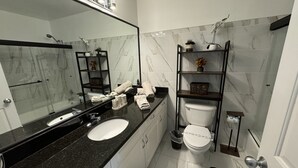 A modern bathroom with a black granite countertop, white marble tiles, a white sink, a toilet, and a black rug. - Villa Crayson (Kissimmee)