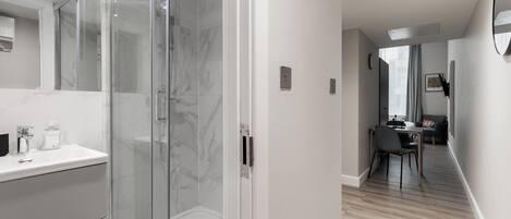 Une salle de bain moderne dotée d’une douche à parois de verre, de carreaux de marbre et d’un plan de toilette blanc avec un lavabo.