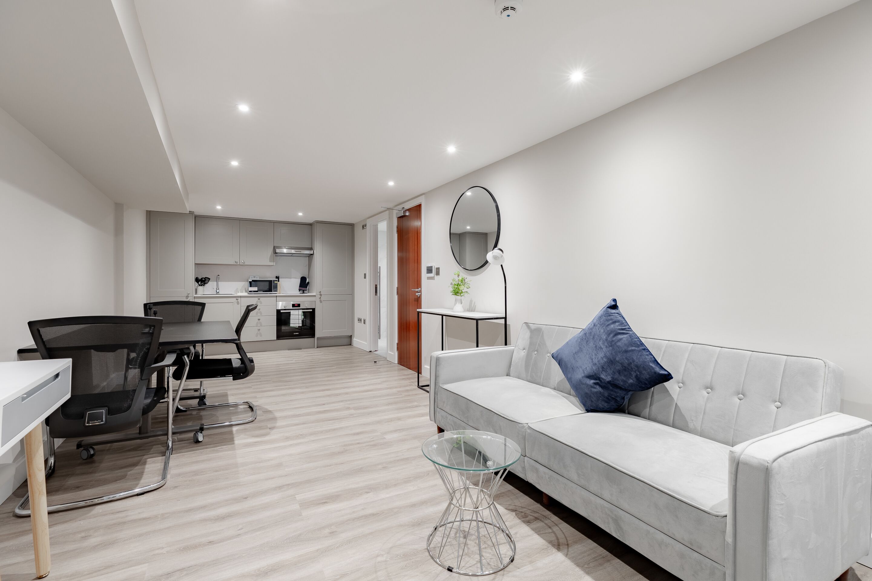 A modern living room with a grey sofa, a glass coffee table, and a dining area with a table and chairs.
