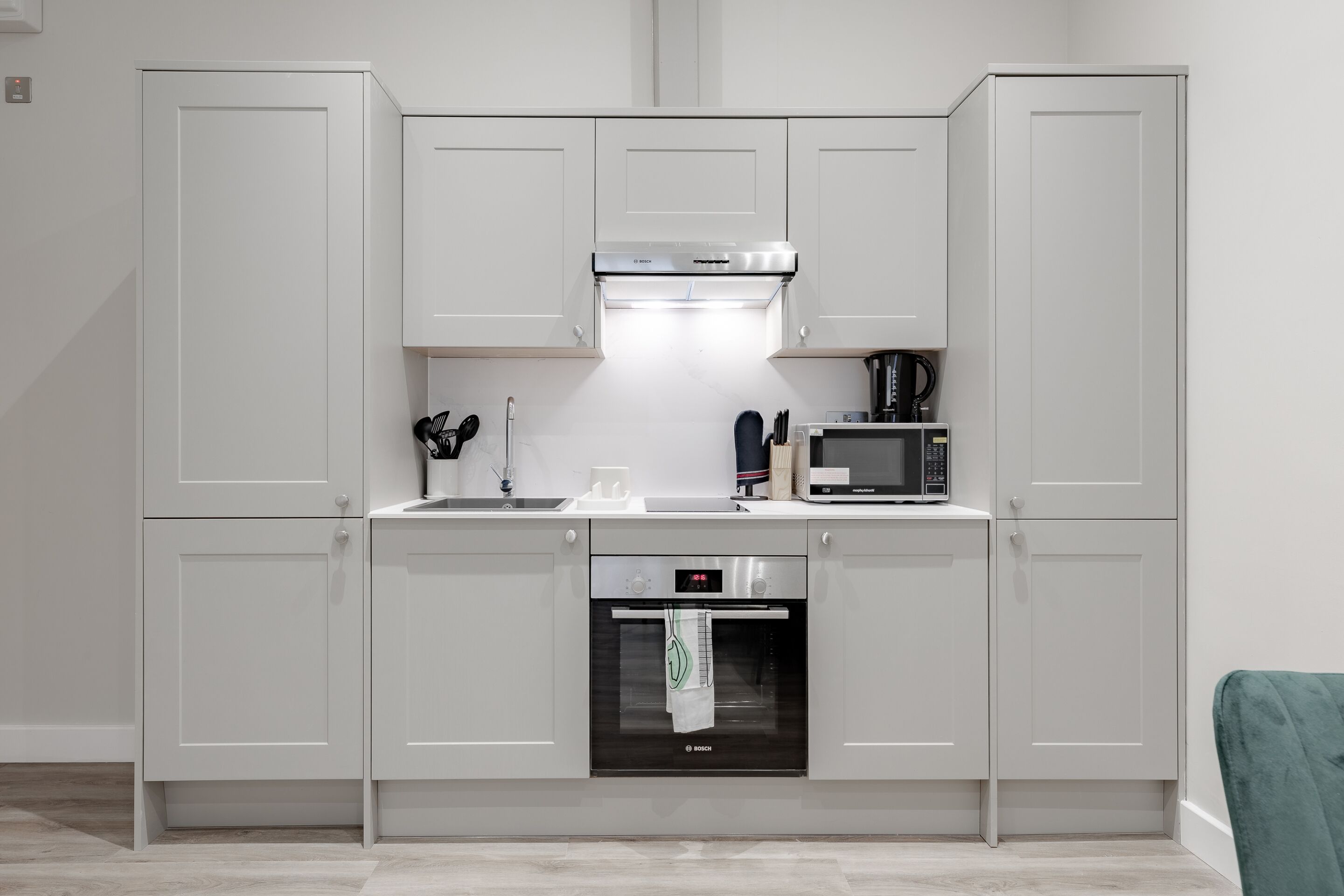 Uma cozinha moderna com armários brancos, forno Bosch, micro-ondas e máquina de café.