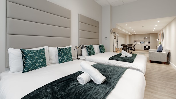 Quarto de hotel com duas camas, uma cozinha compacta e um espaço de estar.