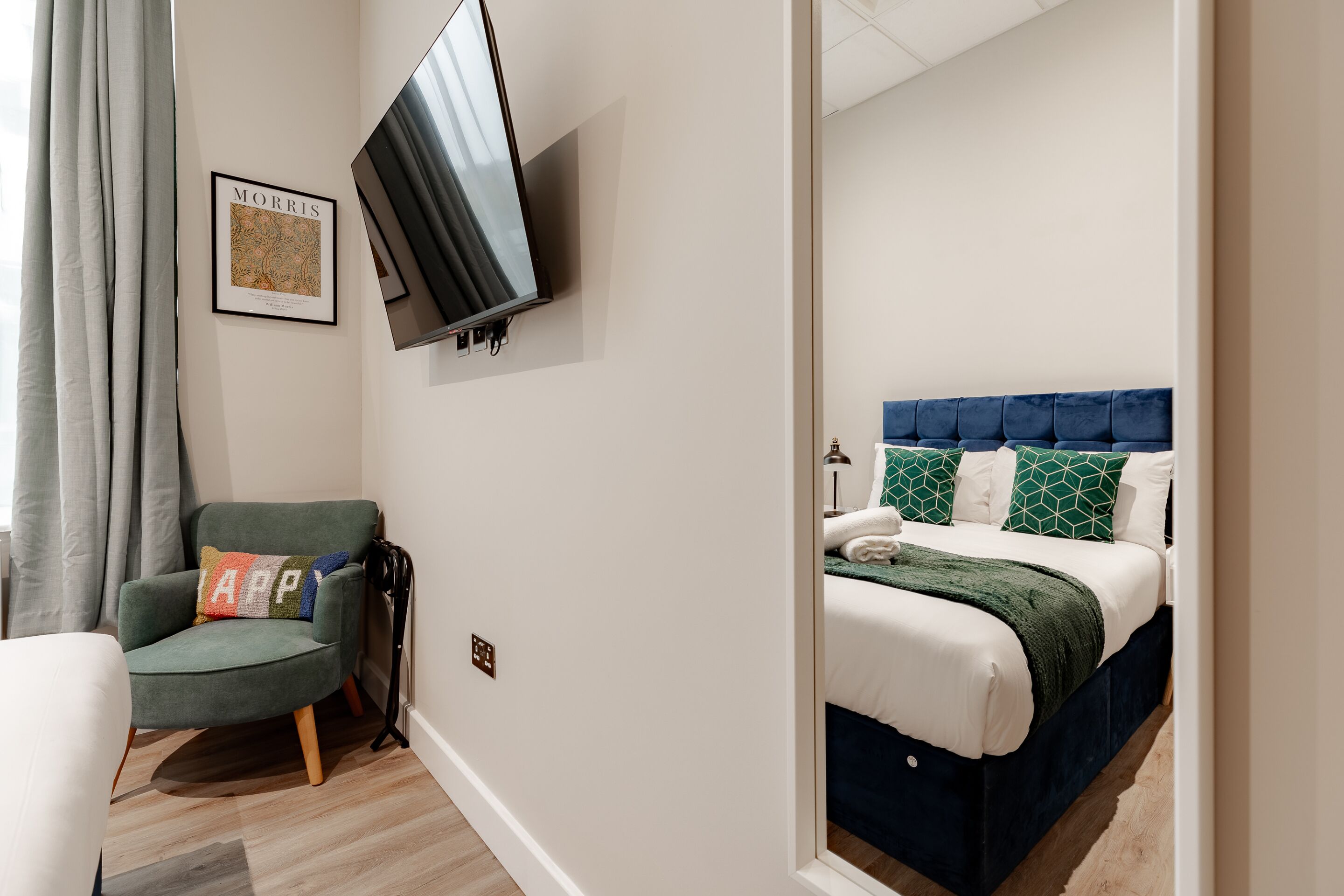 Una habitación de hotel moderna con una cama, una silla, un televisor de pantalla plana y un cuadro en la pared.