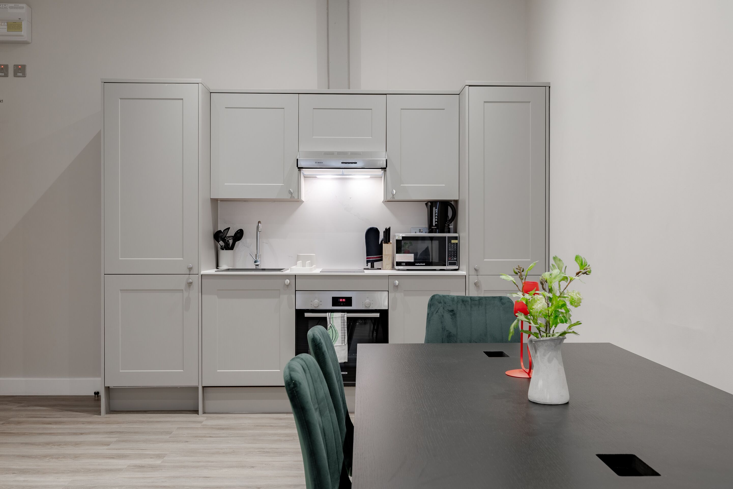 Cozinha moderna com armários brancos, micro-ondas e forno. Há uma mesa de jantar com cadeiras e um vaso com flores.