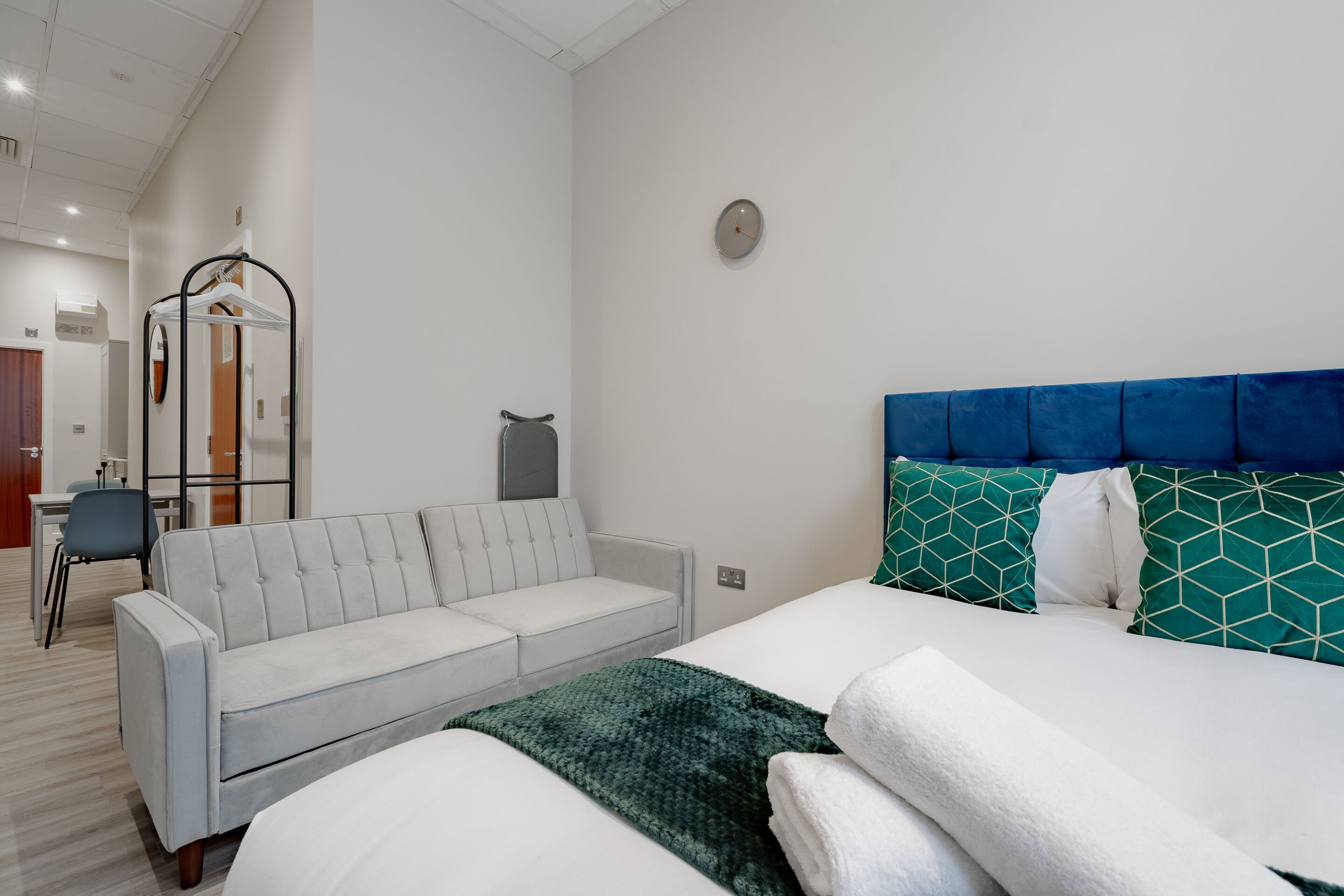 Une chambre d’hôtel moderne avec un lit, un canapé gris, un bureau et un miroir.