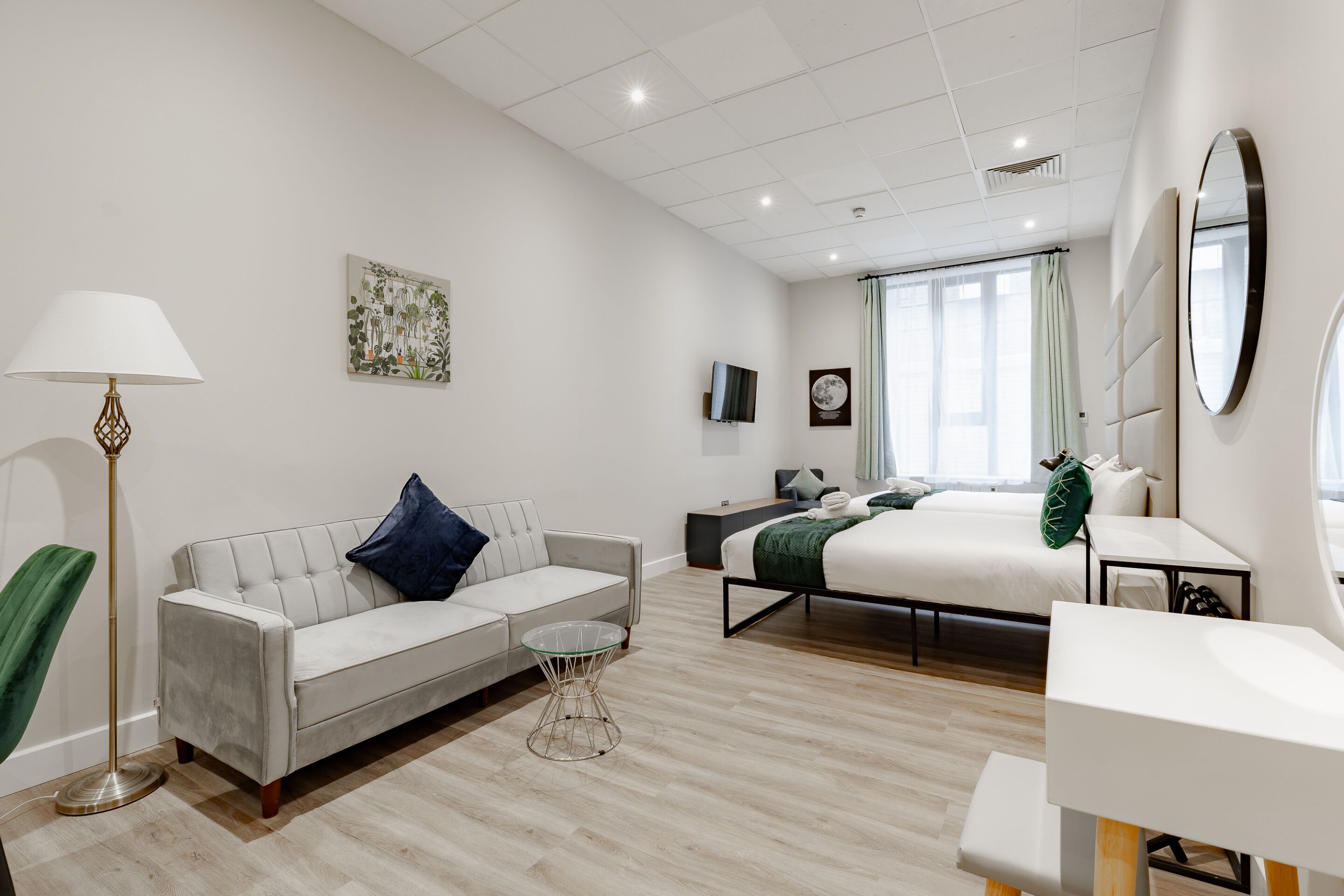 A modern hotel room with a sofa, a bed, a small table, and a TV.