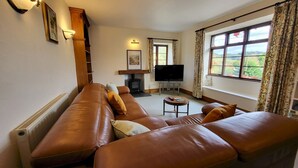 Una sala de estar con un sofá de cuero marrón, televisor, chimenea y una ventana con cortinas.