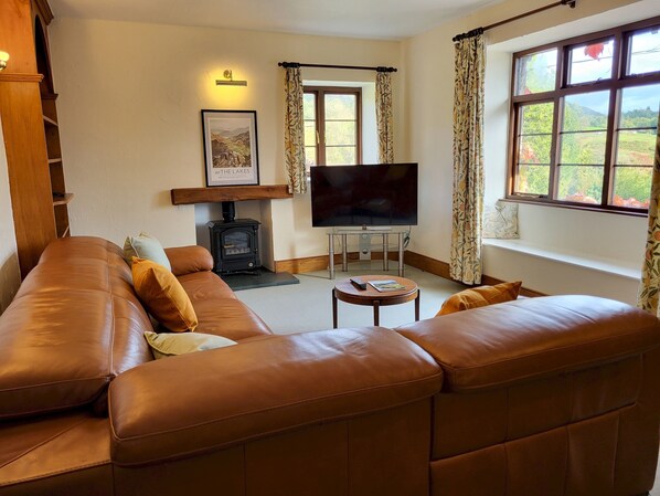 A cozy living room with a leather sofa, a fireplace, a television, and a window with curtains.