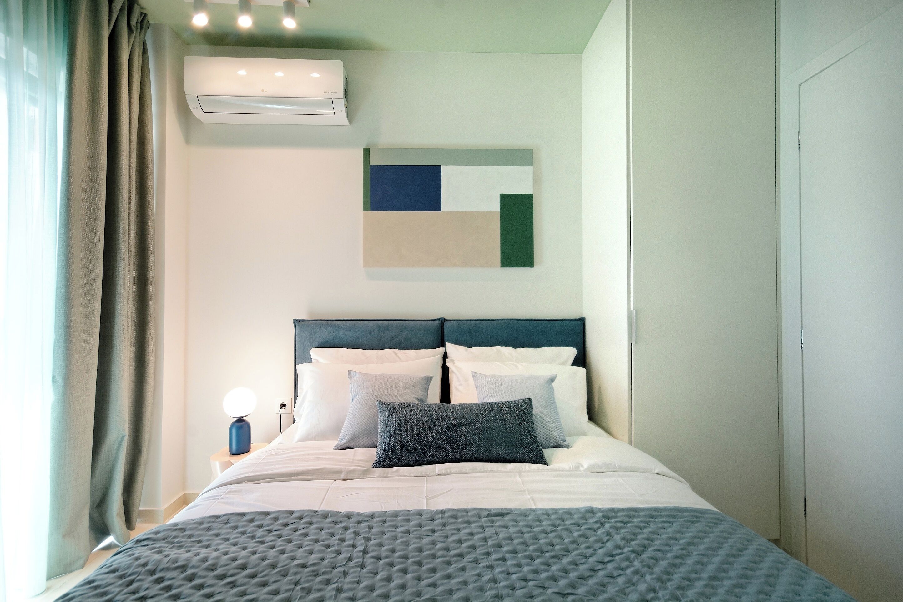 A neatly made bed with a tufted headboard, a bedside lamp, and a wall-mounted air conditioner.