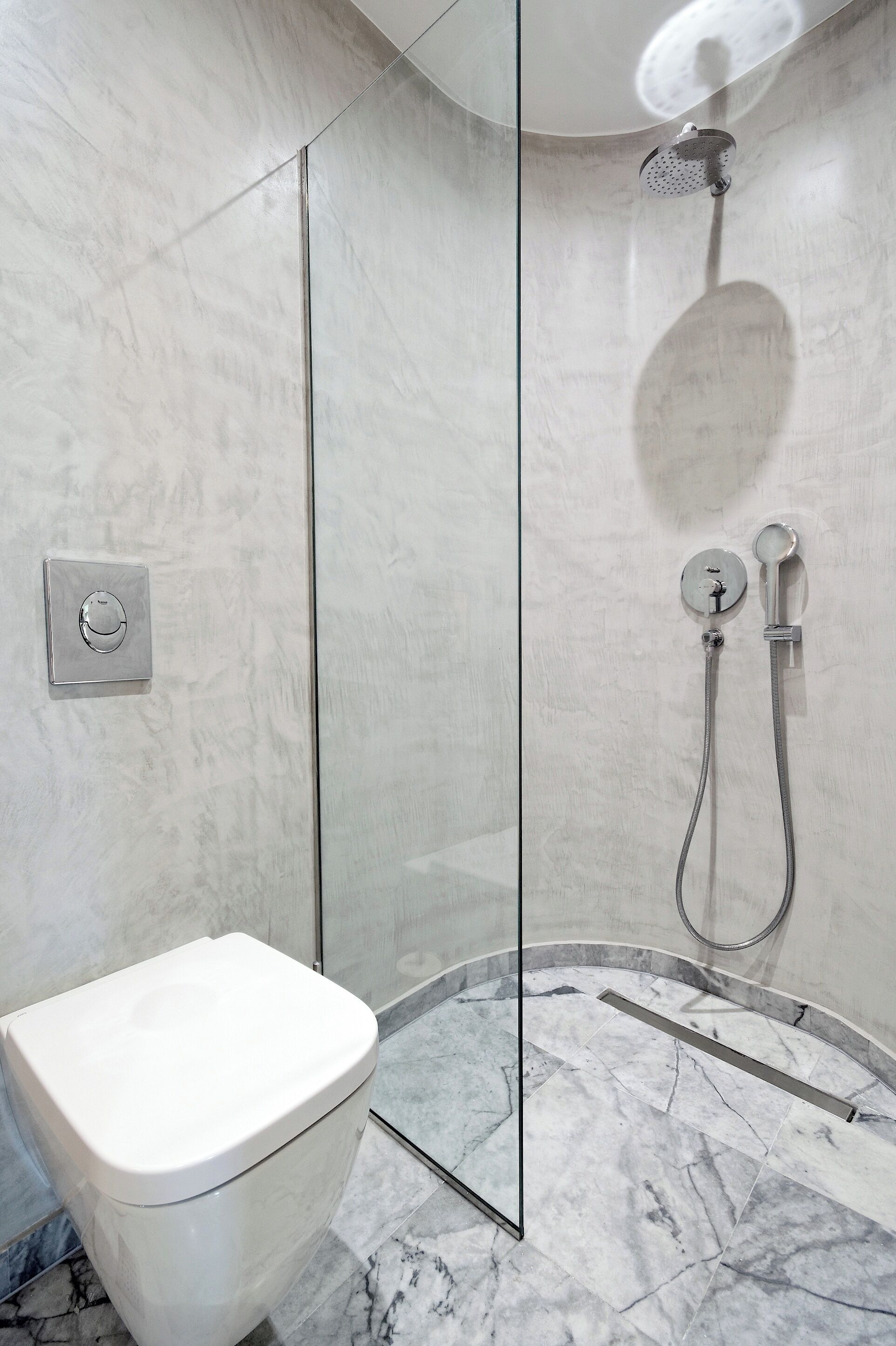 Un baño moderno con ducha envuelta en vidrio, inodoro y suelo de mármol.
