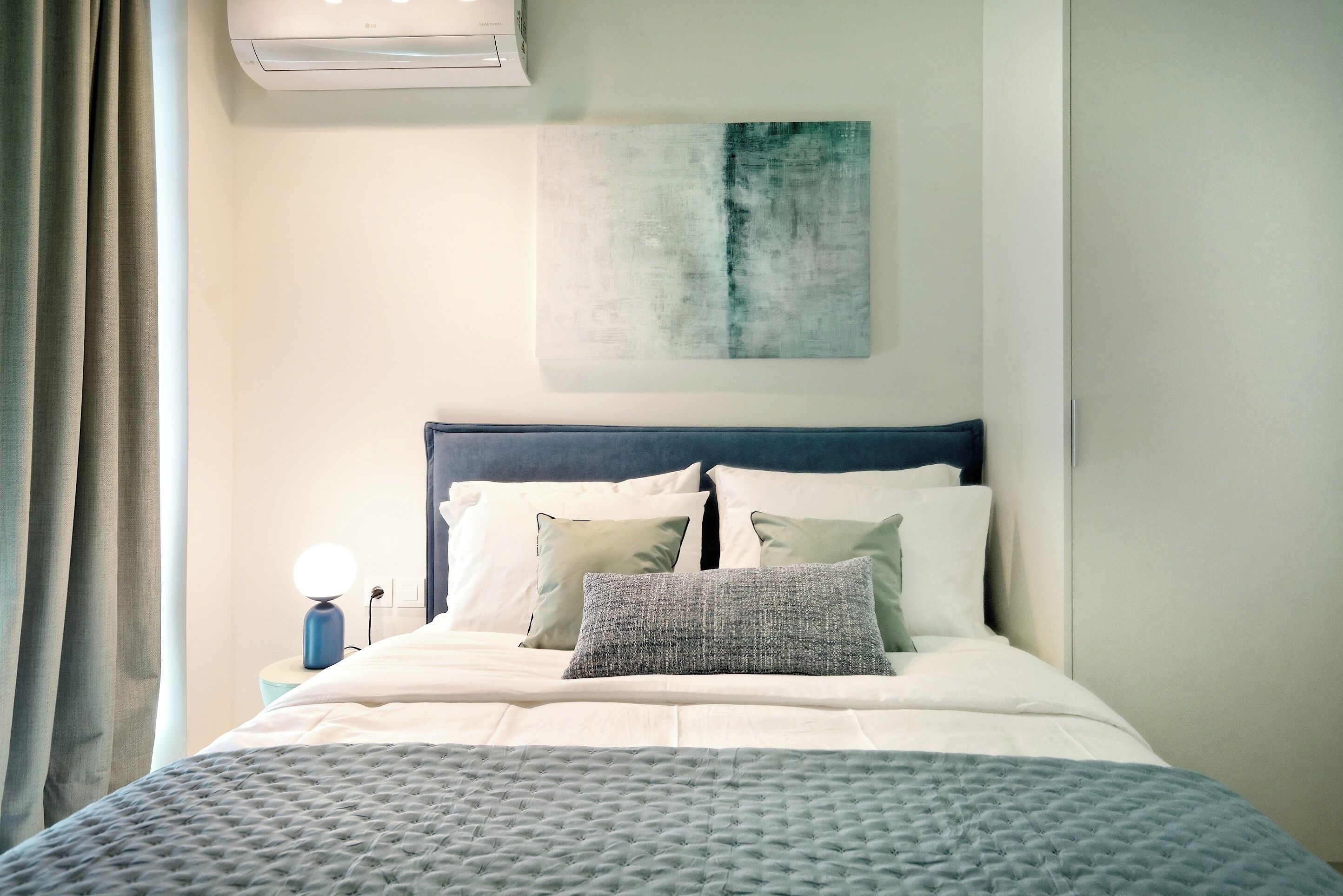 A neatly made bed with a blue headboard, white bedding, and a textured grey throw blanket.