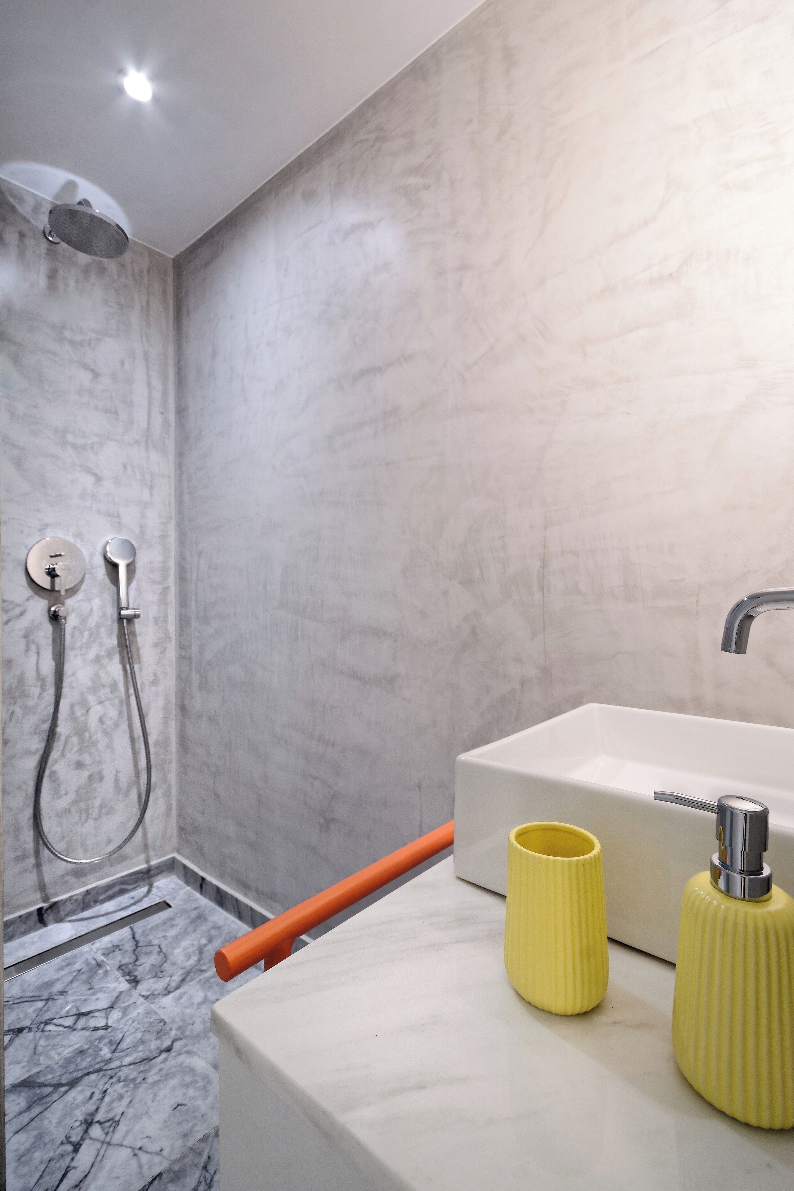 Une salle de bain avec une douche, un lavabo et deux récipients jaunes posés sur le comptoir.