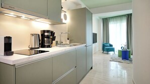 A modern kitchen with a built-in stove, coffee maker, and sink. There is a blue chair and a small table with a checkered rug in the living area.