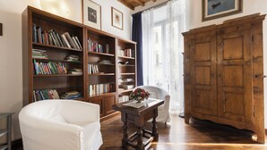 A room with a wooden floor, a white armchair, a wooden bookshelf, a wooden cabinet, and a table with a vase. - Sauro River View by MMega (Florence)