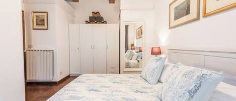 A bedroom with a wooden ceiling, a bed with floral bedding, a wardrobe, a radiator, and framed pictures on the walls.