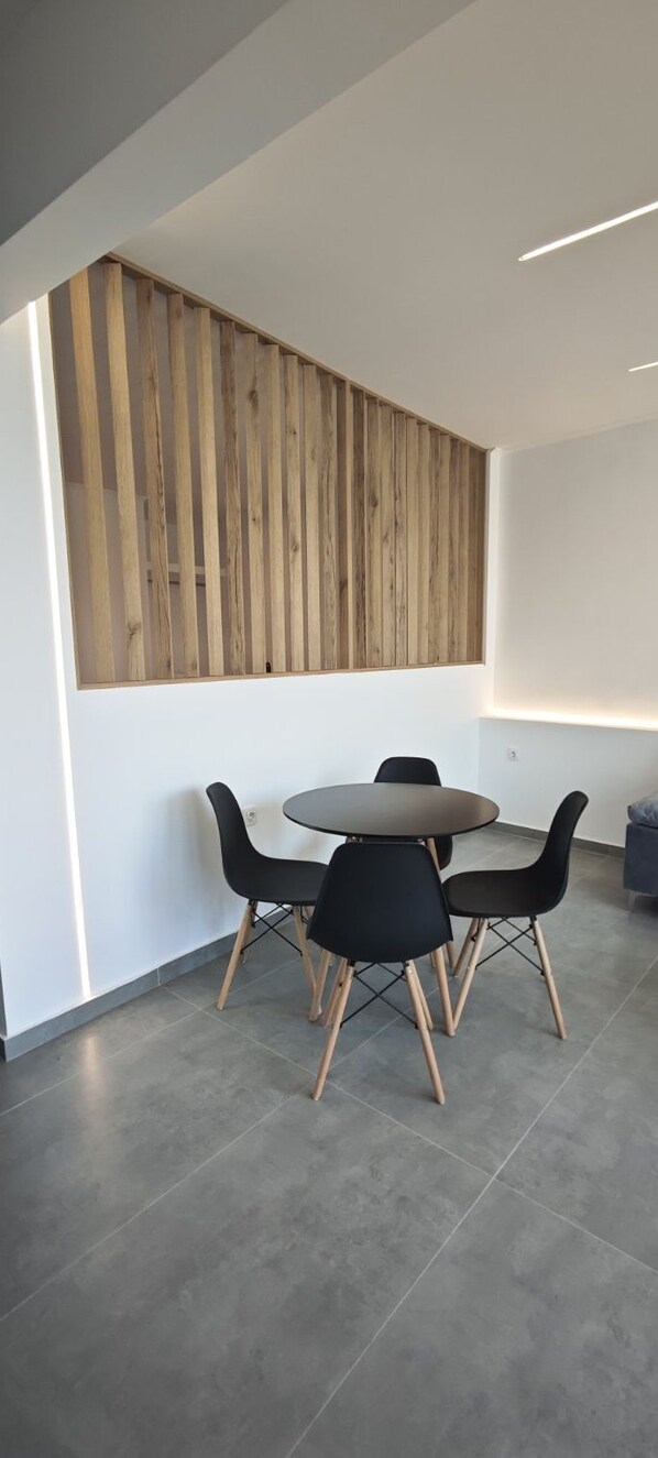 Ein moderner Essbereich mit einem runden Tisch, vier Stühlen, einer Wand aus Holzleisten und einer Deckeneinbauleuchte.
