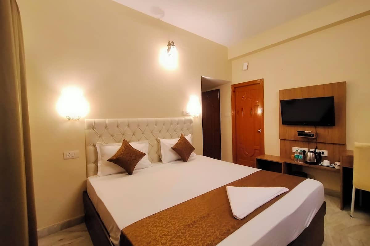 A hotel room with a large bed, a television mounted on the wall, and a desk with a kettle and cups.