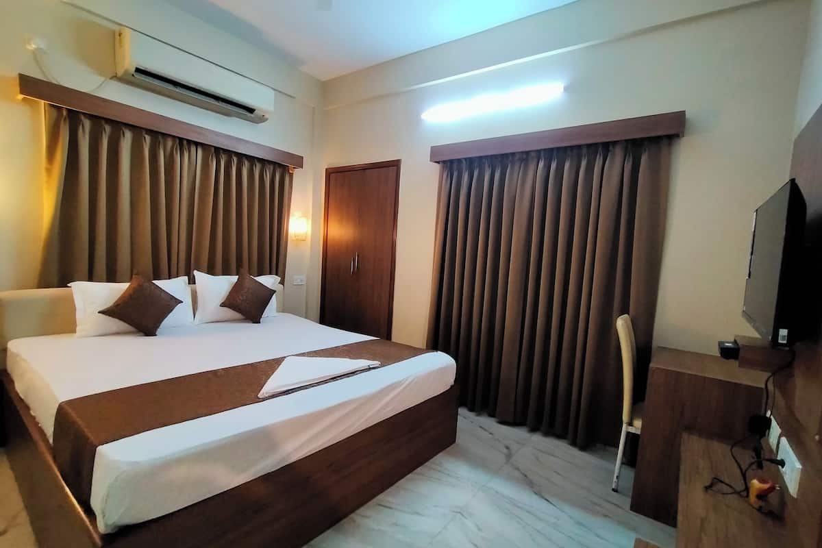 A hotel room with a large bed, a flat-screen TV, an air conditioning unit, and a wooden headboard.