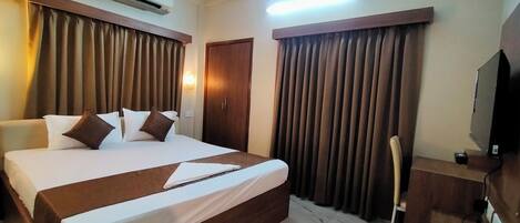 A hotel room with a large bed, a flat-screen TV, an air conditioning unit, and a wooden headboard.