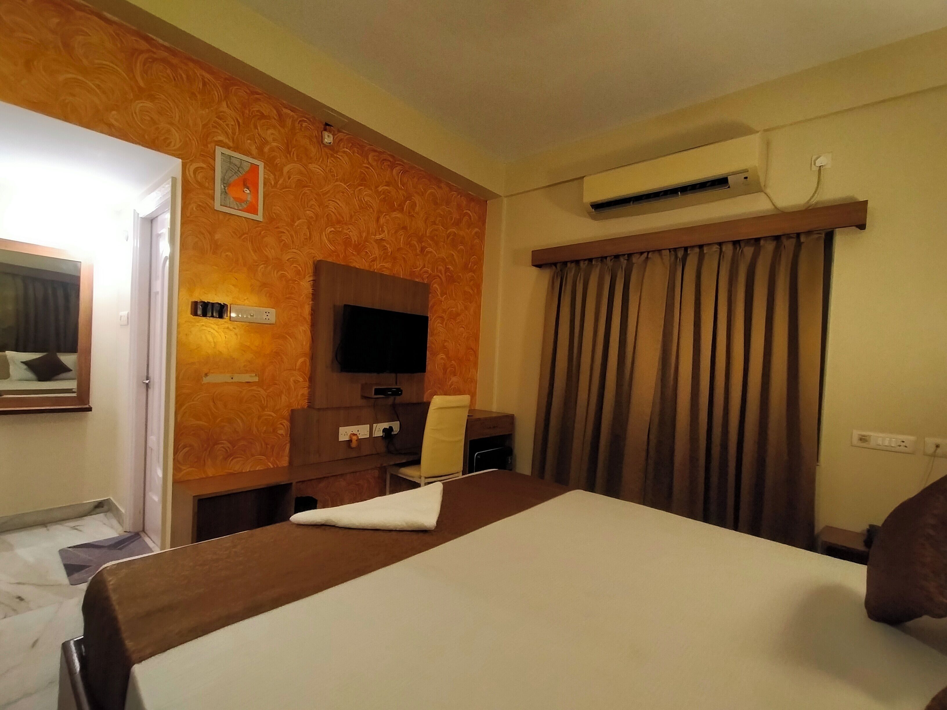 A hotel room with a bed, a TV mounted on the wall, an air conditioner, and a window with curtains.