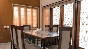A dining area with a marble table and wooden chairs, large windows with curtains, and a decorative metal gate. - Ashray The Living Entity  (Bidhannagar)