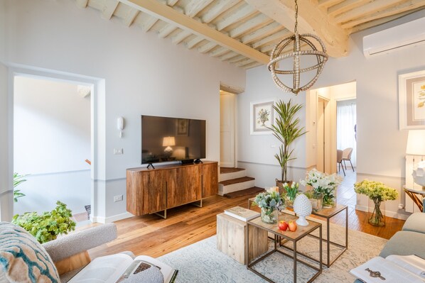 Un salon moderne avec un meuble TV en bois, un grand téléviseur à écran plat, un coin repas avec une table et des chaises, et un escalier menant à une autre pièce.