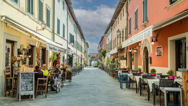 Une rue pavée bordée de cafés et de restaurants, avec des terrasses et des tables à l’extérieur.