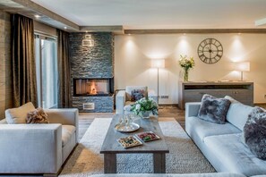 A modern living room with a stone fireplace, two sofas, a coffee table with food, and a clock on the wall.