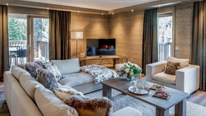 A modern living room with a sofa, armchairs, a coffee table, and a TV. - Wifi, 150m from ski slopes, 1st floor, view mountain, sauna, terrace, balcony, fireplace or stove (Courchevel)