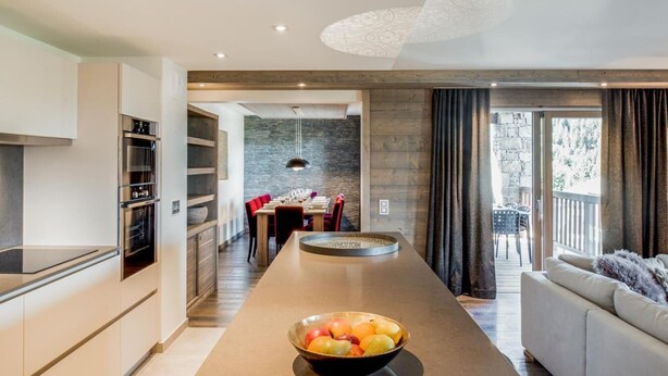 A modern kitchen with built-in appliances, a central island with a fruit bowl, and a dining area with red chairs. - Wifi, 150m from ski slopes, 1st floor, view mountain, sauna, terrace, balcony, fireplace or stove (Courchevel)
