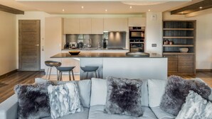 A modern kitchen with a central island, bar stools, and a built-in oven. - Wifi, 150m from ski slopes, 1st floor, view mountain, sauna, terrace, balcony, fireplace or stove (Courchevel)