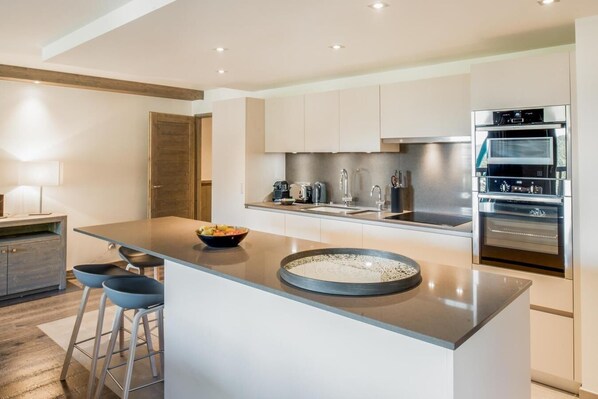 A modern kitchen with a central island, stainless steel appliances, and bar stools.