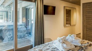 A bedroom with a bed, a TV mounted on the wall, and a large window with curtains. - Wifi, 150m from ski slopes, 1st floor, view mountain, sauna, terrace, balcony, fireplace or stove (Courchevel)