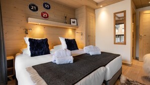 Habitación de hotel con una cama grande, dos almohadas, una manta y toallas sobre la cama. Paredes de madera y un espejo en la pared.